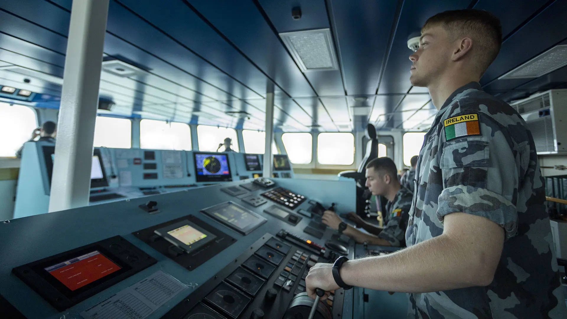 Naval officers operating navigation and communication systems on a ship’s bridge, monitoring radar and control panels during maritime operations.