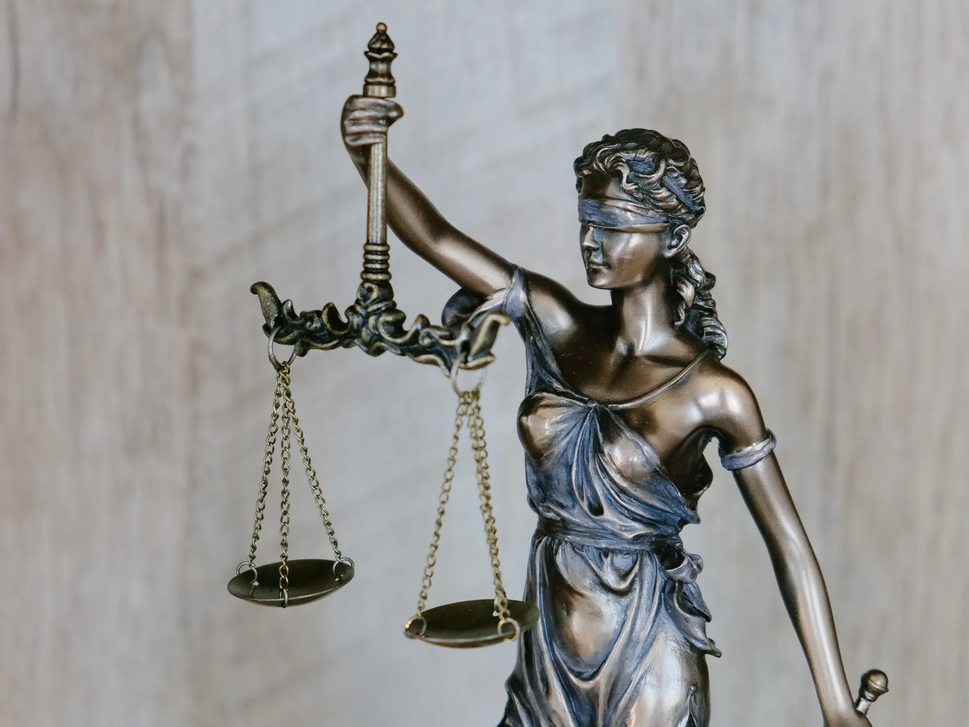 Bronze statue of Lady Justice holding scales, symbolizing fairness and impartiality, with a blurred background of wooden texture."
