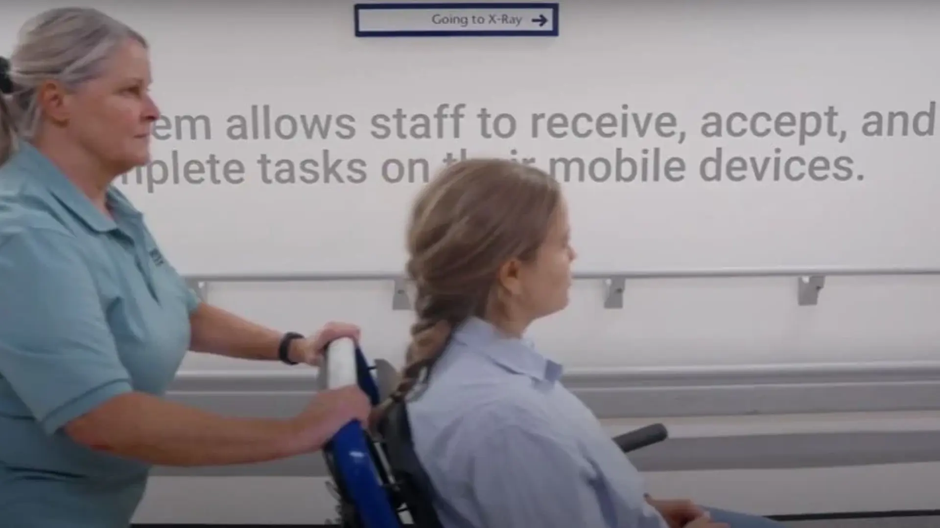 Hospital staff member pushes a patient in a wheelchair through Queen Elizabeth University Hospital, illustrating the use of Columna Flow Task Management for mobile task coordination.